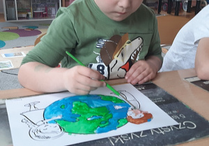 Bartuś maluje farbami plakatowymi planetę Ziemię.